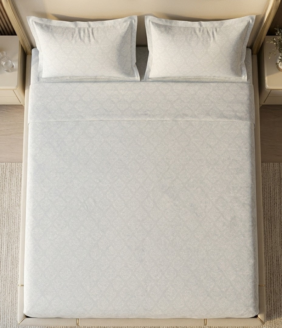 Bed with light gray bedding and pillows on a wooden floor.